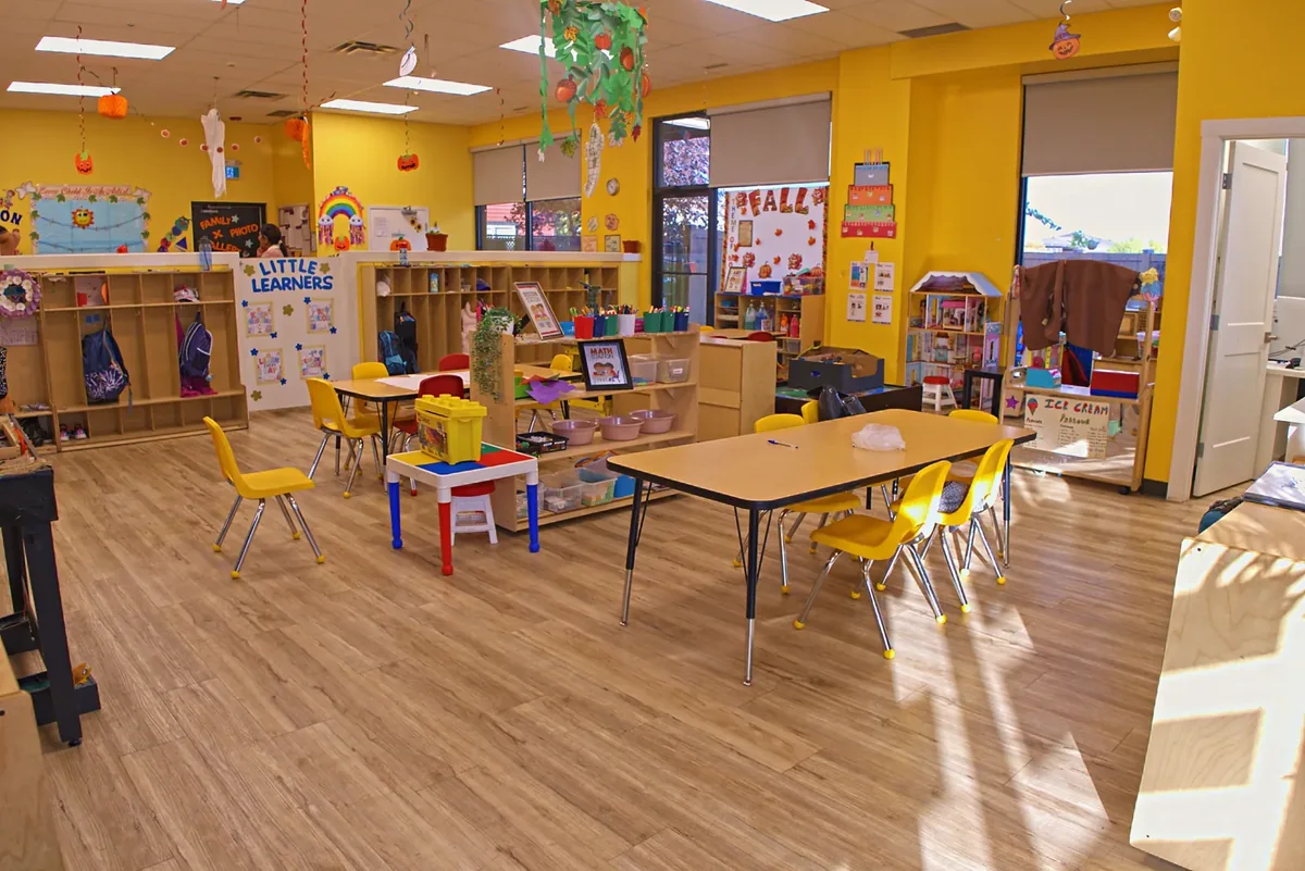 A bright empty classroom at Little Otters Daycare in Leduc, with low tables, yellow chairs and coat cubbies